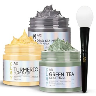 Set of three clay masks with a brush, including turmeric, Dead Sea mud, and green tea varieties.