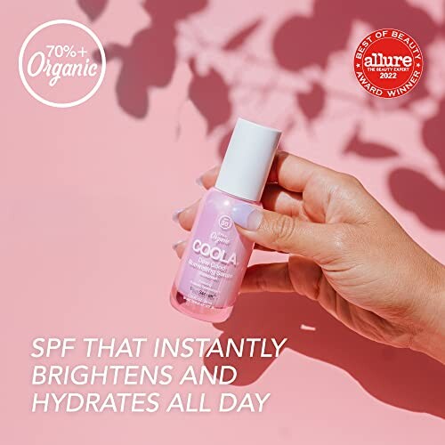 Hand holding Coola organic SPF serum against pink backdrop.