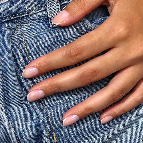 Hand with neatly manicured nails resting on denim jeans pocket.