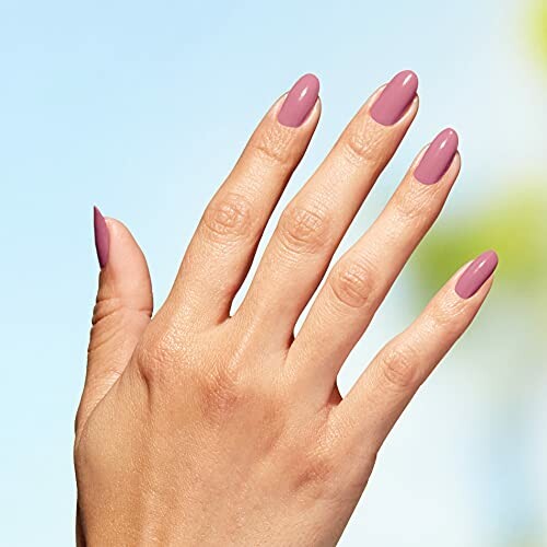 Hand with pink nail polish against a blurred background.